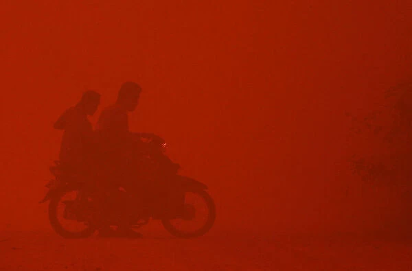 A motorcyclist turns back due to intense heat while passing through haze near burnt peat land in