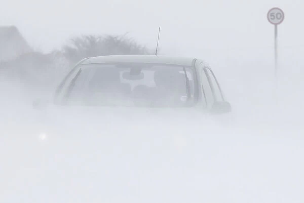 A motorist drives through snow blown from fields near Buxton in central England