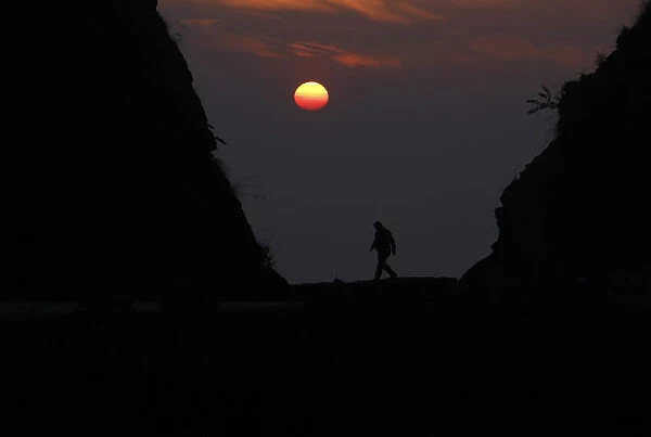 A Nepalese man is silhouetted by the setting sun as he walks along the hills at Kailali