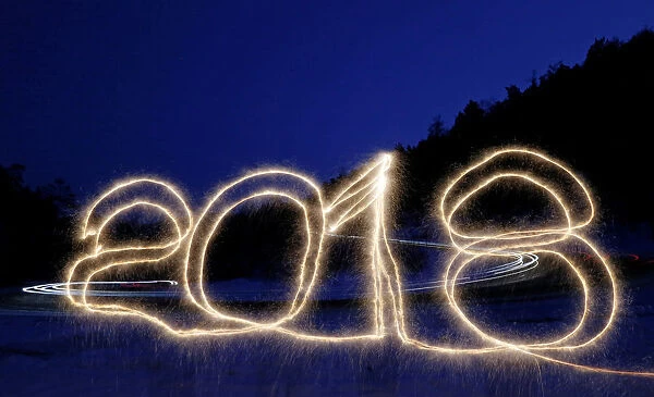 The numbers 2018 are written in the air with a sparkler on a roadside while cars drive