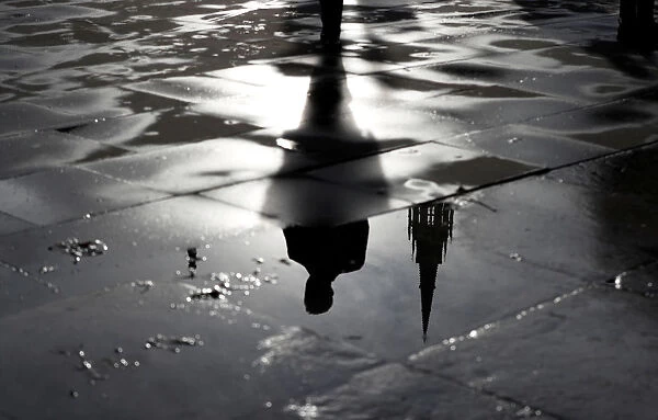 The Palace of Westminster and a man walking are reflected in a puddle in London