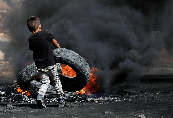 A Palestinian boy puts a tyre on fire during clashes with Israeli troops near the Jewish