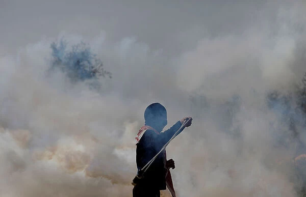 Palestinian demonstrator returns a tear gas canister fired by Israeli troops during
