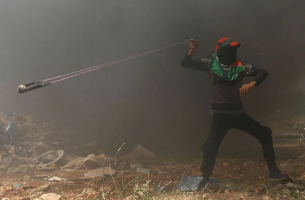 Palestinian demonstrator uses a sling to hurl stones at Israeli troops during a protest