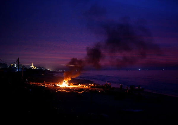 Palestinian fishermen warm themselves by a fire at a beach on a winter day