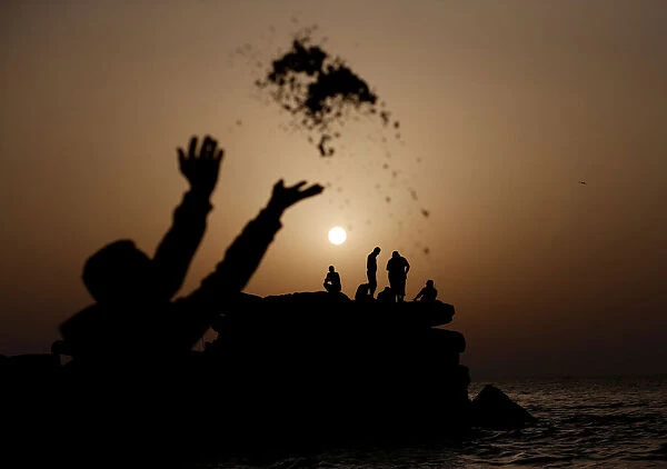 Palestinian throws sand during sunset, at the seaport of Gaza City