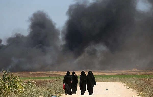 Palestinian woman walk as smoke rises during a protest against U. S