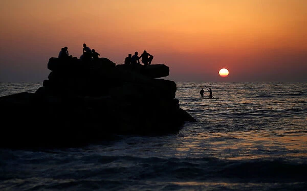 Palestinians ride a boat in the Mediterranean Sea as others enjoy the beach during sunset