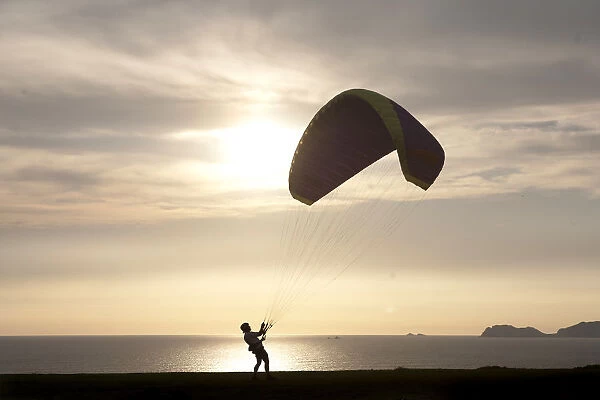 A paragliding instructor arranges his paraglide at the ocean-front in the neighbourhood