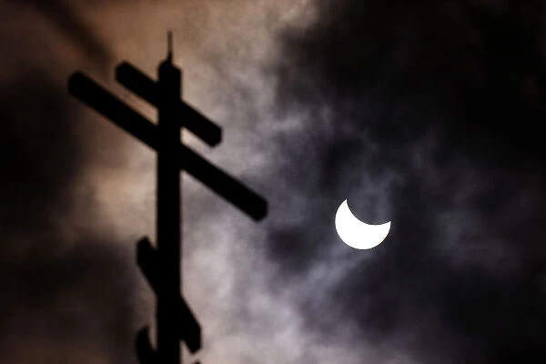 A partial solar eclipse forms in the sky through clouds near the cross of the Church of
