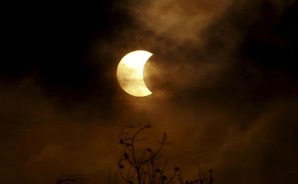 A partial solar eclipse is seen through clouds in Bangkok