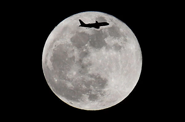 A passenger plane flies in front of a supermoon full moon over London