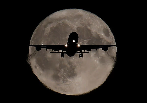 A passenger plane, with a full Harvest moon seen behind, makes its final landing approach