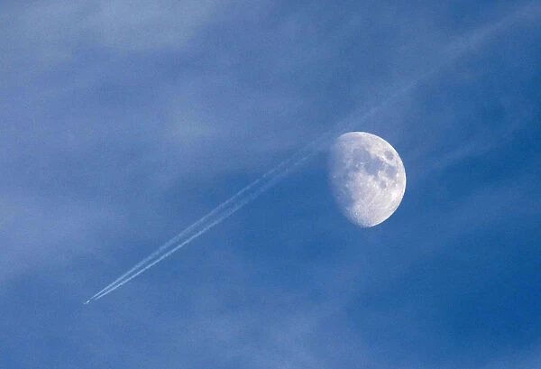 A passenger plane leaves a contrail as it flies past the moon over Malta