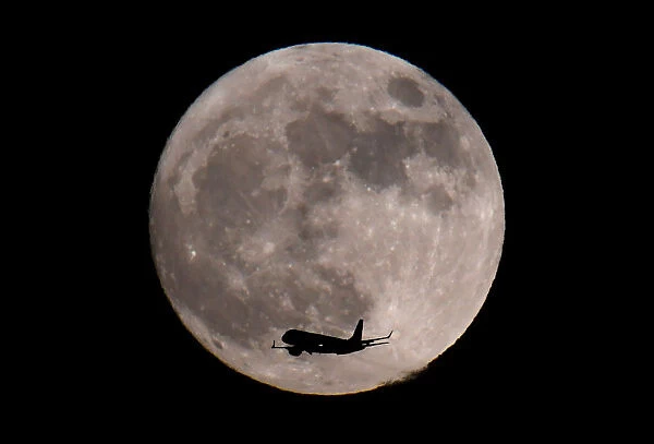 A passenger plane, with a supermoon full moon seen behind, makes its final landing