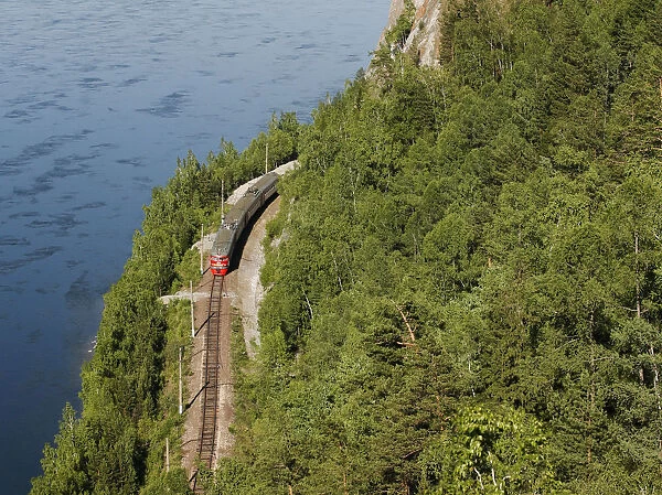 A passenger train moves along a railway along the bank of the Yenisei River near the