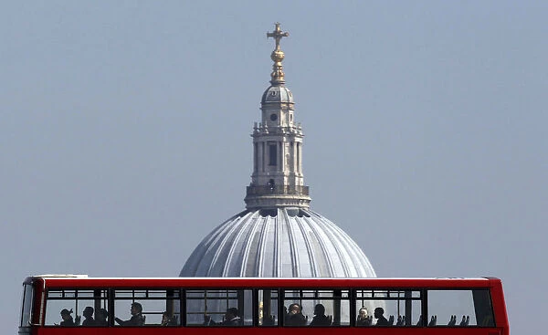 Passengers travel on the top deck of a bus as it is driven past St Pauls Cathedral