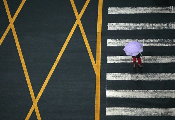 A pedestrian holding an umbrella walks across a main intersection on a rainy day in