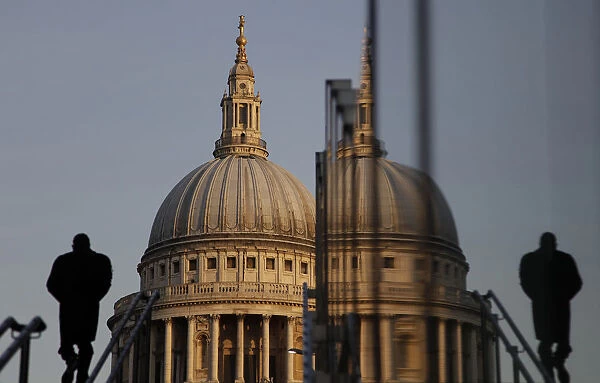 A pedestrian is reflected in glass as he walks towards St Pauls Cathedral in the