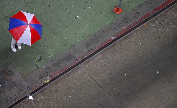 A pedestrian stands under an umbrella while waiting for a bus during a spring rain