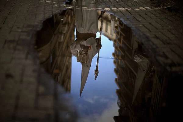 A penitent is reflected in a puddle of water after rain fell at the Humildad brotherhood