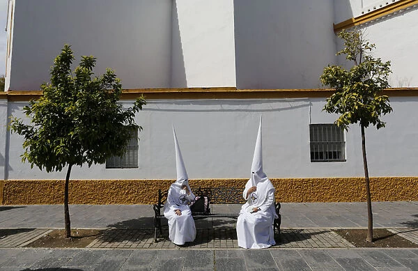 Penitents of San Gonzalo brotherhood sit as they wait to take part in a Holy Week