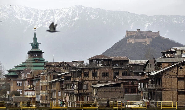 People cross a footbridge in front of cluster of traditional houses in Srinagar