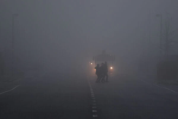 People cross a road in front of a truck in heavy fog in Belfast