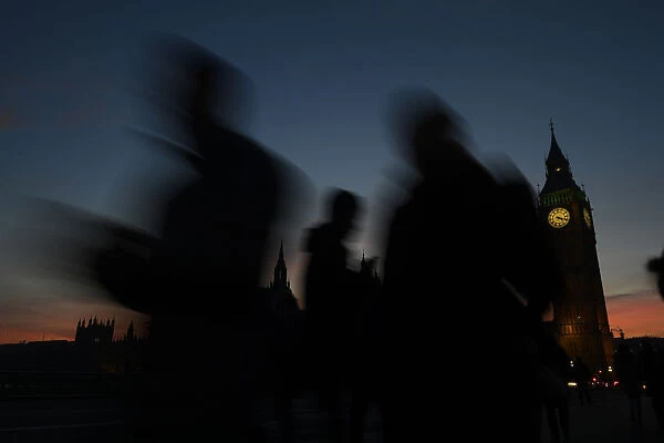 People cross Westminster Bridge as dusk falls behind the Houses of Parliament on a clear