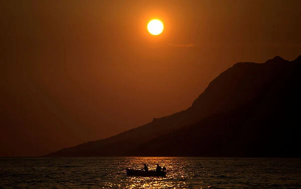 People fish in the Adriatic sea during sunset in Brela, Croatia