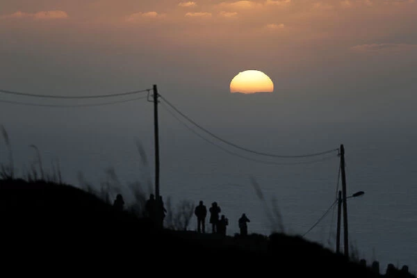 People gather to watch the sunset after a surf session at Praia do Norte in Nazare