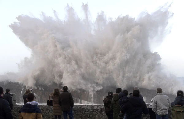 People look and take pictures of giant waves in the port town of Llanes