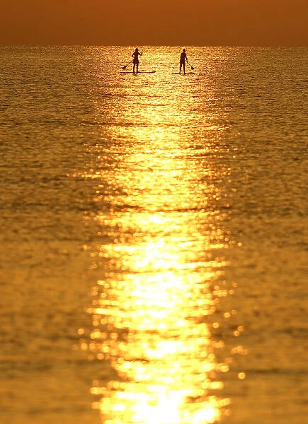 People paddle on a stand-up board during sunrise in a beach in Larnaca