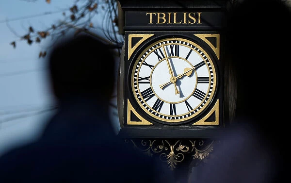 People pass by a clock on the street in Tbilisi