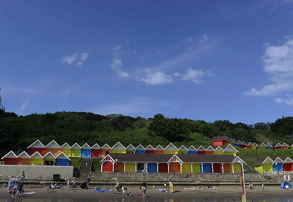 People relax in front of beach huts in the North Bay in Scarborough