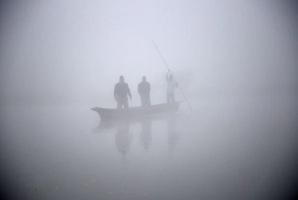 People ride on a boat to reach the bank of Rapti River during the foggy winter morning at
