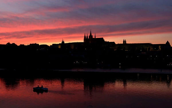 People ride a pedal boat on the Vltava River as the sun sets over the Prague Castle in