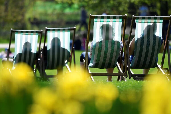 People are silhouetted against the fabric of deckchairs as they enjoy the sunshine in St