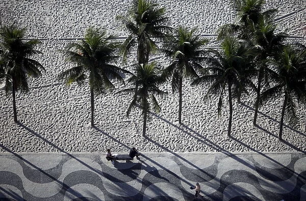 People sit on a bench on the sidewalk at Copacabana Beach in Rio de Janeiro, Brazil