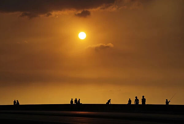 People sit along Havanas seafront boulevard El Malecon during sunset