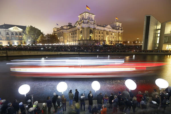 People stand outside the Reichstag lower house of parliament builiding under lit balloons