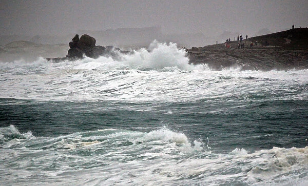 People standing on the Pointe de la Torch peninsula watch waves breaking on the Brittany