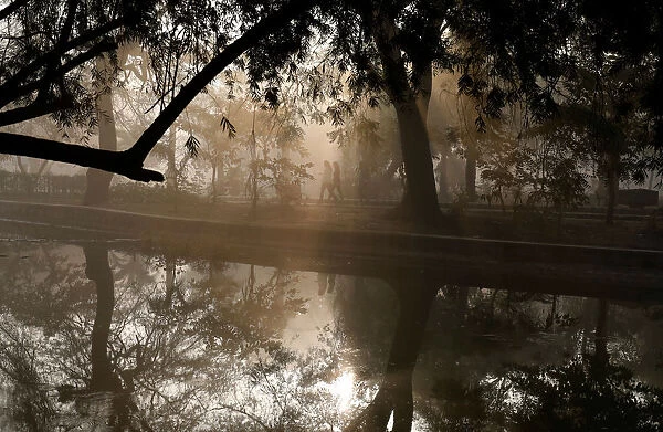 People walk by a lake at a public park on a foggy winter morning in New Delhi
