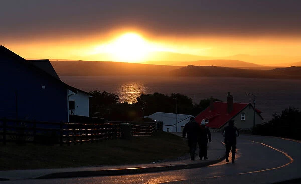 People walk down a road at sunset in Port Stanley