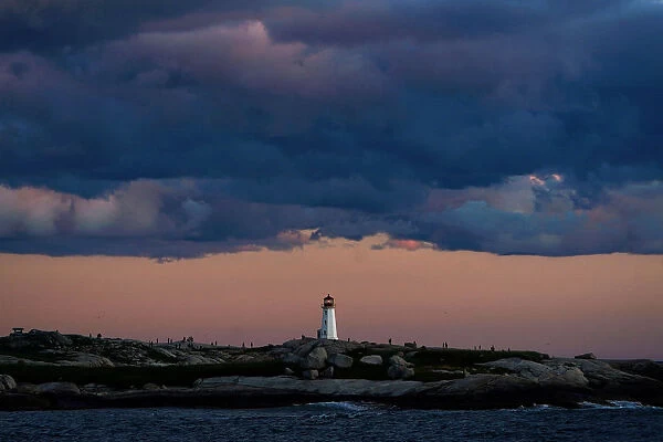 People walk on the rocks at the lighthouse at dusk in Peggys Cove