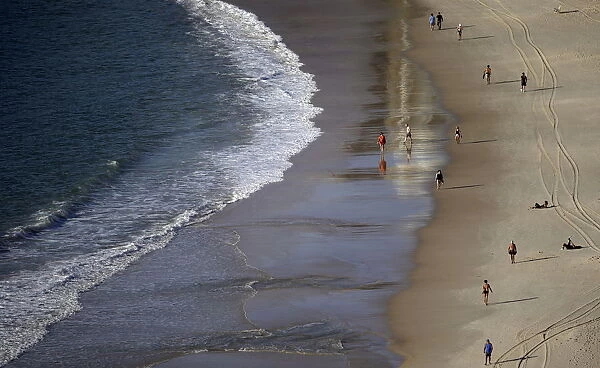 People walk on the shoreline of Copacabana Beach in Rio de Janeiro, Brazil