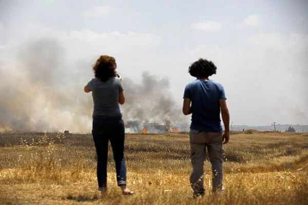 People watch a burning field, on the Israeli side of the border fence between Israel
