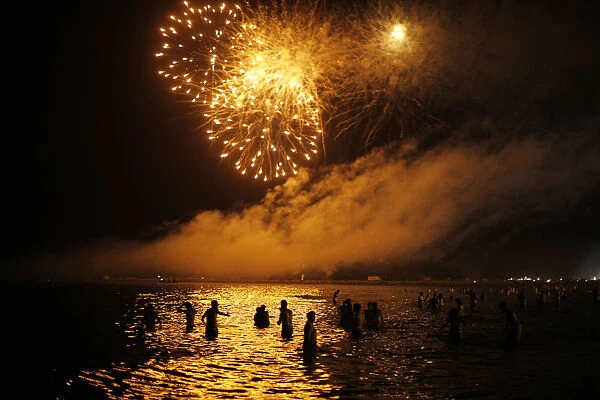 People watch fireworks as they take a bath in the Mediterranean Sea on San Juan s