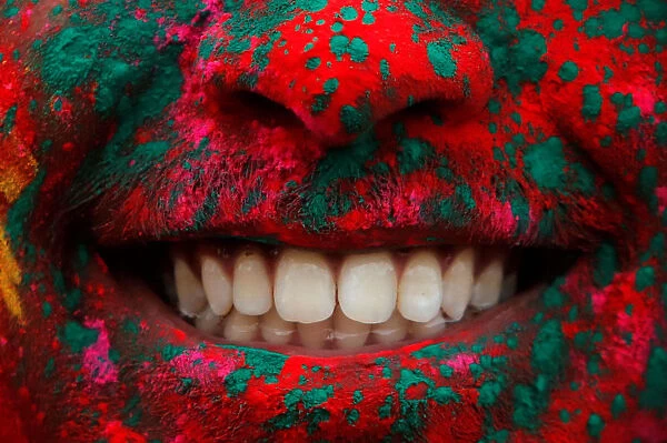 A person smiles after being covered in colored powder during a Holi festival party