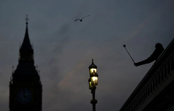 A person takes a photograph on Westminster Bridge at dusk in central London